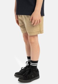 Khaki shorts med rak passform, kombinerade med svarta sneakers med vita accenter. Svartvita randiga strumpor ger en avslappnad känsla.