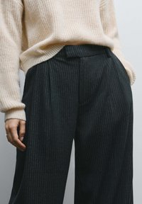 Pantalon à jambes larges avec un motif à fines rayures sombres, doté d'une taille haute et de plis, associé à un pull en maille crème texturé.