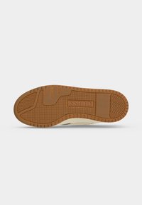 Semelle de chaussure en caoutchouc marron avec motifs de grip texturés et le mot "GUESS" embossé au centre.