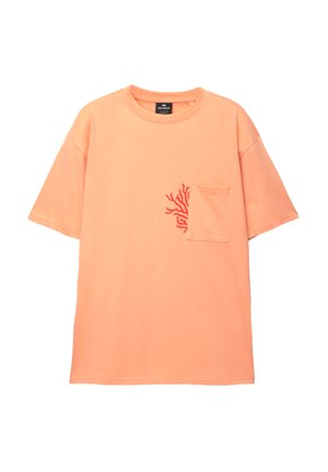 Rövid ujjú, oversize póló őszibarack színű pamutból, piros korall mintával a mellzsebin; kerek nyakkivágás és laza szabás.