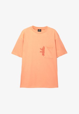 Oversized tričko s krátkým rukávem v broskvové barvě z bavlny s červeným korálovým vzorem na kapsičce; kulatý výstřih a uvolněný střih.