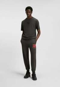 Completo sportivo grigio scuro composto da una t-shirt a maniche corte e pantaloni affusolati con logo rosso "HUGO", caratterizzato da una vestibilità rilassata e una texture liscia.