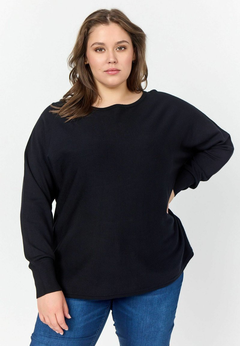 Maglione nero oversize con maniche lunghe, polsini a coste, scollatura rotonda e texture morbida, indossato sopra jeans in denim blu. Design semplice.