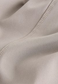 Gros plan sur un tissu beige montrant une couture double surpiquée détaillée et une texture tissée lisse avec des plis doux.