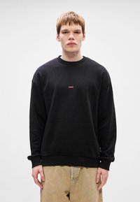 Μαύρο φούτερ από μαλακό υλικό, με στρογγυλή λαιμόκοψη και χαμηλούς ώμους. Κόκκινο λογότυπο "HUGO" κεντραρισμένο στο στήθος.