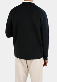 Svart stickad cardigan med spetsig krage, l�ånga ärmar och avslappnad passform. Har en liten röd accentlogotyp nära fållen.