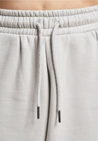 Light gray sweatpants with an elastic waistband, featuring a drawstring with metal aglets and a smooth texture.