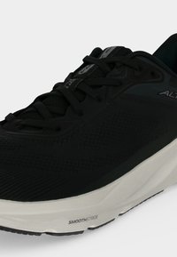 Gros plan d'une chaussure de sport noire avec des lacets noirs et une semelle blanche portant le label "SmoothStride."