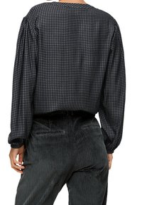 Blouse à motif pied-de-poule noir et gris avec des manches longues, un col rond et un tissu texturé, associée à un pantalon en velours côtelé foncé.