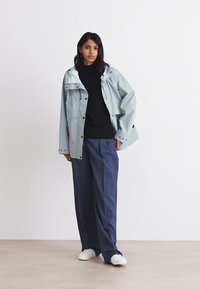Rain jacket in light blue with a hood, snap closures, and a relaxed fit, paired with dark pants and white sneakers. Simple design and texture.