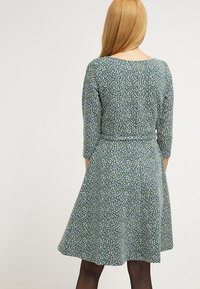 Vihreä mekko, jossa on tiukka yläosa ja levenevä hame. Siinä on valkoisista ja sinisistä kuvioista koostuva design, kolmanneksen pituiset hihat ja sileä pinta.