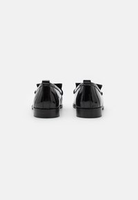 Een paar glanzende zwarte leren loafers met lage hakken, gezien vanaf de achterkant op een plain witte achtergrond.