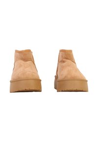 Bottines à talon en suède beige tanné, avec un bout arrondi, une surface texturée et une semelle épaisse en caoutchouc. Le design comprend un col court élastiqué.