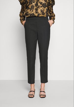 Personne portant un pantalon noir sur mesure longueur cheville, un chemisier marron avec imprimé floral noir et des sandales noires à talons ouvertes.