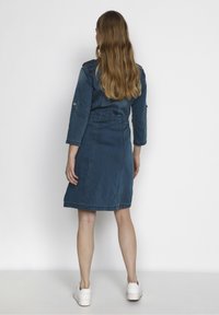 Tummansininen farkkumekko, jossa on kolme neljännesosaa hihat, vyötärö on kiristetty ja helma yltää polveen. Mukana näkyvät ompeleet ja napit.