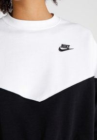 Svart och vit sweatshirt med ett chevron-mönster, med rund hals och en liten svart Nike-logotyp på bröstet. Mjuk tygtextur.