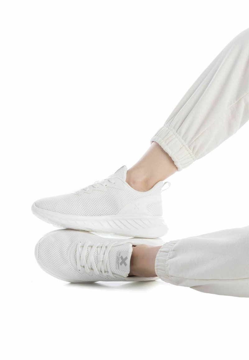 Zapatillas deportivas blancas con parte superior de malla, diseño texturizado y suela acolchada. Combinadas con joggers ligeros y elásticos con puños.