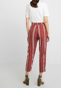Pantalon rayé rouge et crème avec une taille élastique, une longueur raccourcie et une coupe décontractée, associé à des sandales à talons vertes.