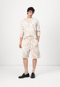 Hellbeige Sweatshirt mit großem Blumenmuster, kombiniert mit passenden Shorts, elastischem Bund und schwarzen Slippern über beigen Socken.