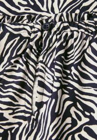 Tkanina w wzór zebry w czerni i bieli o miękkiej teksturze. Posiada zapięcie na guzik w pasie oraz plisowane detale.