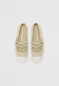 Zapatillas de lona beige con doble tira y hebillas plateadas, suelas de goma rosa y punteras blancas, con el logotipo de Converse en el interior.