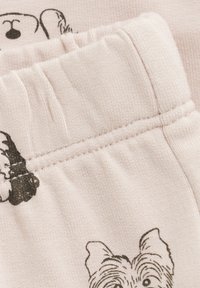 Jasnoróżowa bawełniana tkanina z ilustracjami czarnych psów. Pas jest elastyczny z widocznym przeszyciem, a tekstura jest miękka i prążkowana.