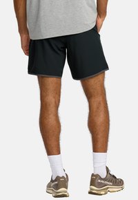 Black athletic shorts with a smooth texture and gray trim, paired with tan sneakers and white socks. Visible leg and shoe details.