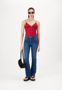 Punane formitud tank top õhukeste rihmadega, sinised laiad teksad, mustad platvormsidurid ja väike must käekott. Selged prillid ja värviline kaelakee.