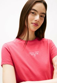 Camiseta de algodón roja con cuello redondo, mangas cortas y texto blanco que dice "Tommy Jeans Nueva York" en el pecho.