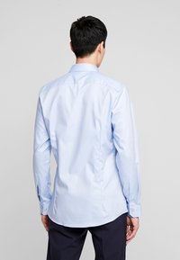 Lichtblauwe overhemd met lange mouwen en een kraag met knopen, gladde textuur, achterpasnaad en knopen bij de manchetten.