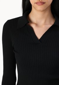 Black ribbed knit top with a collared neckline, featuring long sleeves and a fitted silhouette. Texture is smooth with vertical lines.