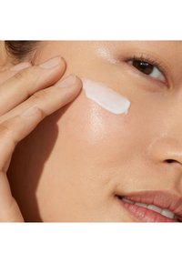 Hydraterende crème aangebracht op een wang, glad en wit van kleur, met een glanzende huidtextuur, die een natuurlijke, evenwichtige huidtint laat zien.