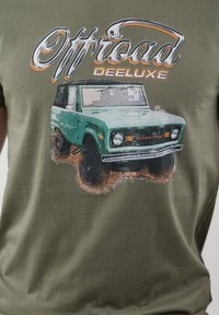 Oliva zelena bombažna majica z obrabljenim grafičnim motivom zelene terenske vozila s črnimi kolesi in napisom "Offroad Deeluxe" zgoraj.