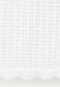 Gros plan d'un tissu blanc tissé texturé avec un bord festonné et un motif quadrillé subtil.