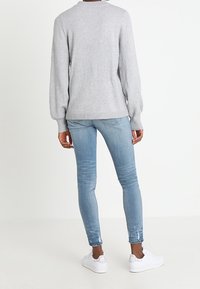 Hellgrauer Strickpullover mit Rippabschlüssen, kombiniert mit mittel-hoch geschnittenen hellblauen skinny Jeans mit Distressed-Details und weißen Sneakern.