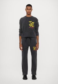 Mørkegrå treningsdrakt med en crewneck sweatshirt med leopardmønster og logo, kombinert med matchende bukser med snøring i livet.