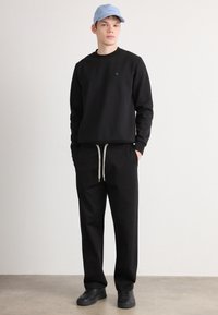 Sort sweatshirt med rund halsudskæring, ribbede manchetter; sorte sweatpants med snor; lyseblå cap; sorte sneakers. Minimalistisk stil.