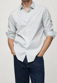 Gestreept overhemd van lichte stof, met verticale blauwe en witte strepen, een kraag en opgerolde mouwen. Draagt men met donkere jeans.