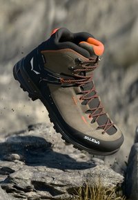 Brązowe buty trekkingowe z pomarańczowymi akcentami, textured materiał, wytrzymała podeszwa i oddychający wierzch. Posiada metalowe oczka i charakterystyczne oznakowanie.