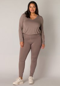 Bruine lange mouw top met een V-hals, gecombineerd met bijpassende strakke legging. Heeft een zachte textuur en een slim fit. Draagt het met witte sneakers.