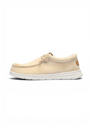 Zapato casual beige tipo slip-on con parte superior de tela suave, detalle de encaje y suela de goma blanca diseñado para comodidad y uso diario.