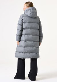 Abrigo de plumas gris con capucha, que presenta secciones acolchadas horizontales, de largo y textura suave, combinado con pantalones de pierna ancha negros.