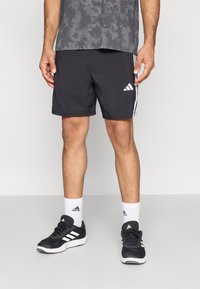 Mustad kergekaalulised spordipüksid valgete küljeribadega. Komplektis mustad jalanõud, valged sokid ja halli mustriga särk.