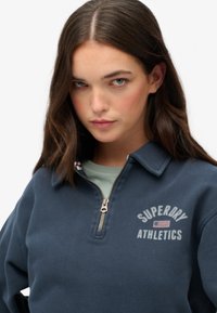 Sudadera de forro polar azul marino con media cremallera que cuenta con un cuello, un pequeño logotipo en el pecho y un acabado texturizado. Cierre de cremallera con un tirador metálico.