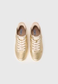 Pair of gold-tone Skechers BOBS Slip-ins sneakers with cream laces, perforated detailing, and padded collars on white background.