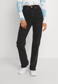 Höga svarta jeans i denim med fem fickor, stängning med stålknapp och rak ben-design. Matchas med vita sneakers.