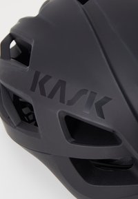 Casque de vélo noir au design aérodynamique, doté de trous de ventilation, d'une finition mat lisse, et arborant le logo "KASK" en évidence.