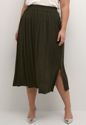 Kvinde iført en mørkegrøn midi-nederdel med sidelængde og elastisk taljebånd, kombineret med sølvfarvede spidse hæle og en hvid indstukket top.