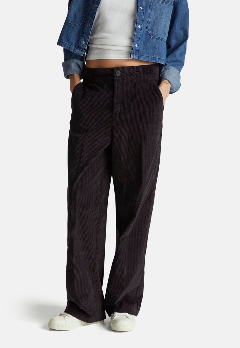 Hnědé kordové kalhoty s volným střihem, s knoflíkovým zapínáním a bočními kapsami, doplněné bílými plátěnými botami.