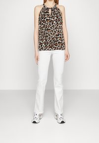 Top senza maniche con stampa leopardata e scollatura a occhiello; tessuto leggero, vestibilità morbida. Abbinato a jeans bianchi a zampa d'elefante e sneakers bianche sportive.